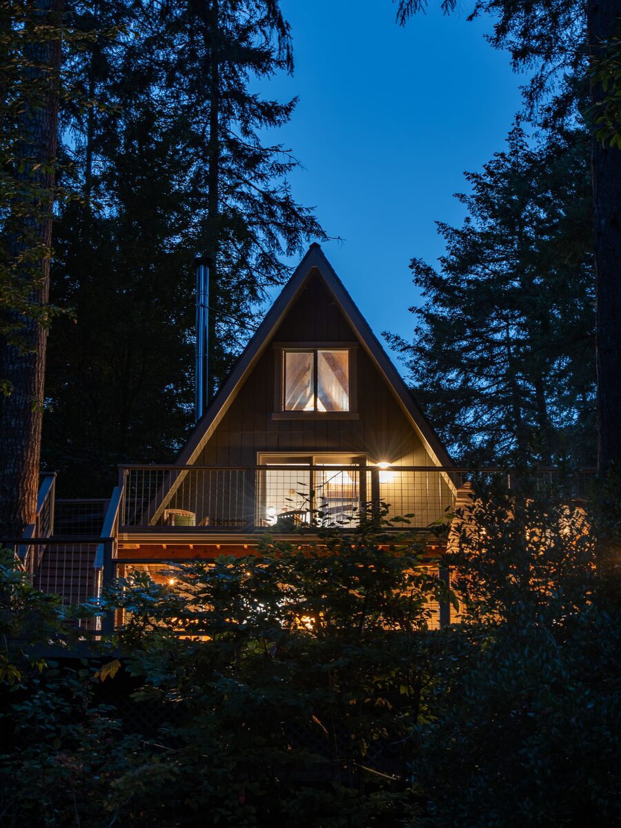 The Minterwood Revival A-frame cabin lit up at dusk among the fir trees in Gig Harbor, Washington