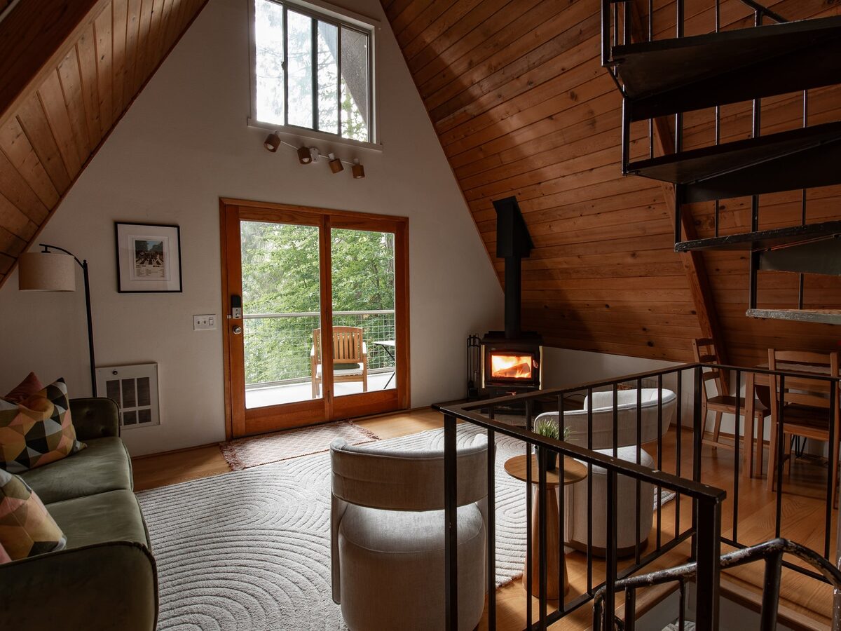 Main level living area with the vaulted A-frame ceiling, tall windows to the lake and the spiral staircase