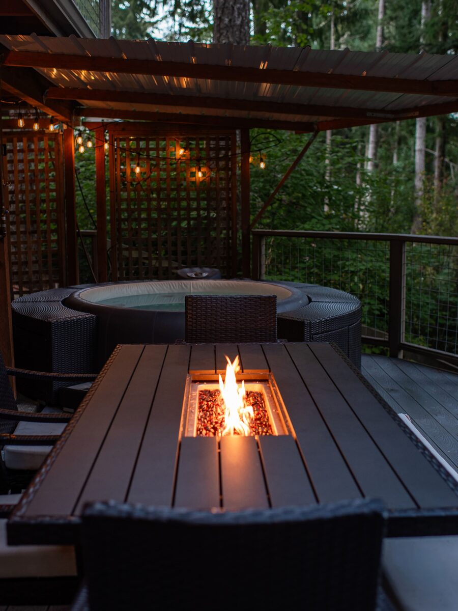 Outdoor dining table with the built-in propane fire pit lit at dusk under string lights