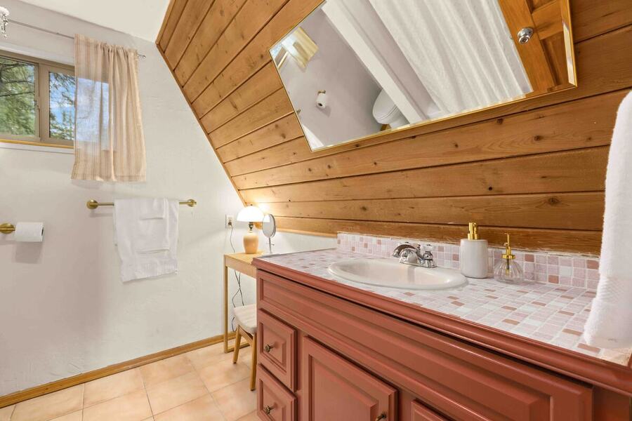 The full bathroom vanity with a wood cabinet and mirror under the sloped cedar ceiling