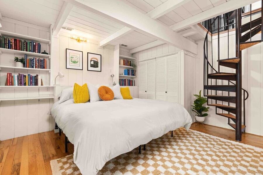 Bedroom one with built-in bookshelves, a checkered rug and the spiral staircase