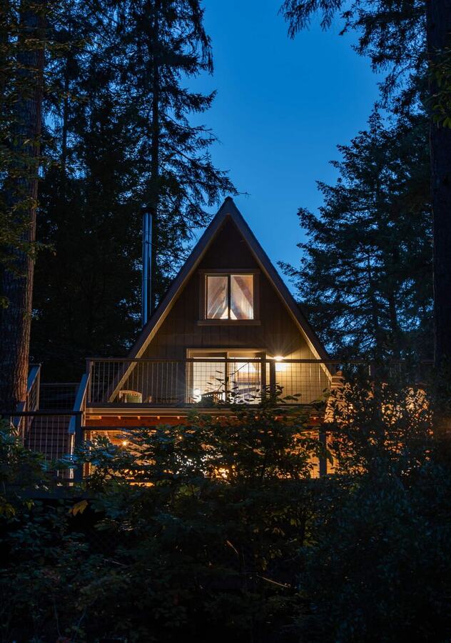 The A-frame at blue hour with the windows glowing through the trees