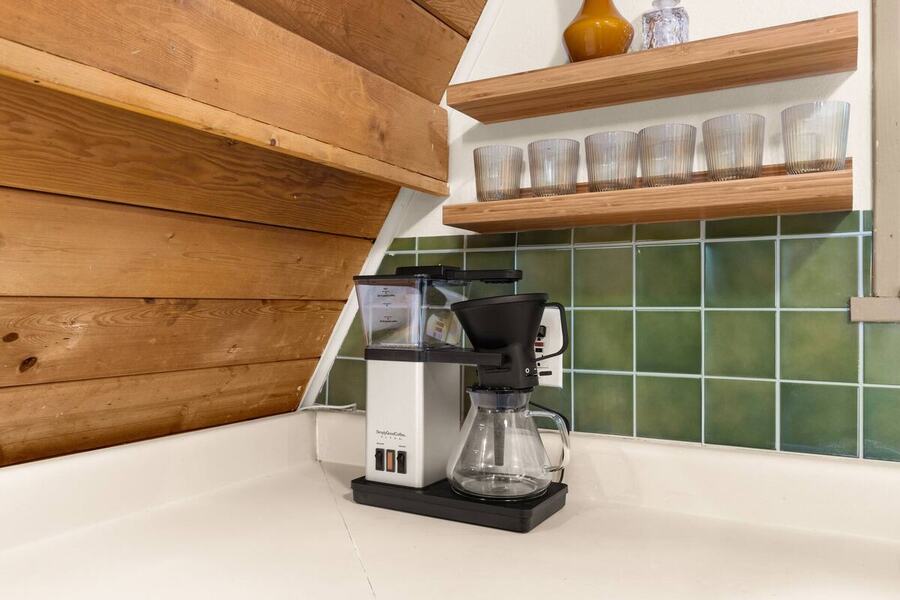 The coffee maker and open shelving against the green tile backsplash