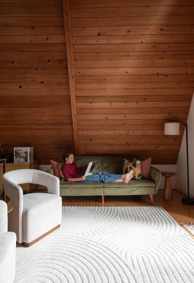 The living room seating with a white armchair, green sofa and cedar A-frame ceiling