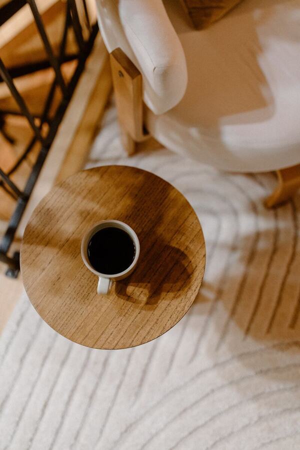 A cup of coffee on the round side table beside the armchair on the wool rug