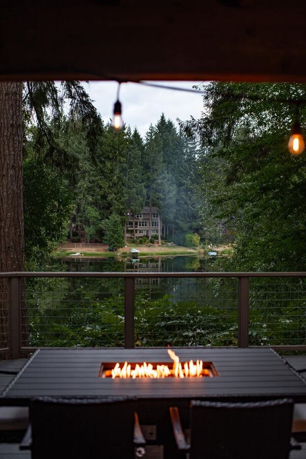 String lights over the covered deck with the fire pit table lit and the lake beyond